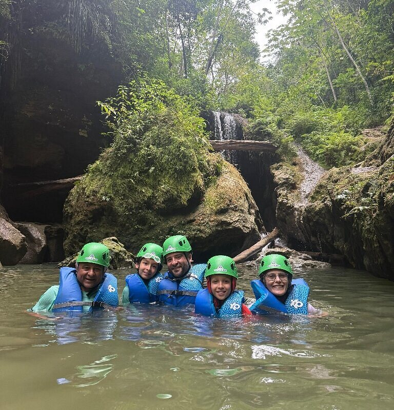 A smiling family in helmets and life vests floating in a jungle river