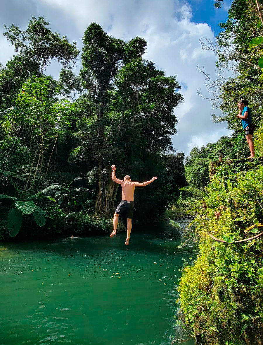 A hiker leaping from a ledge into a jade-green river in the rainforest
