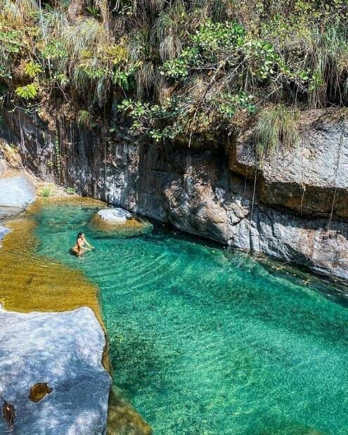A swimmer in a clear turquoise river pool beneath a rock wall